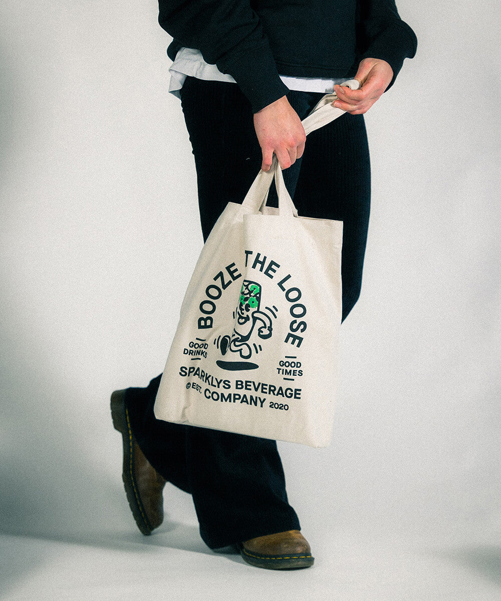 Weibliches Model posiert stolz mit dem Sparklys Tote Bag, der das Vintage-Logo von 'Sparklys Premium Hard Seltzer' und die Vintage-Comic-Stil Grafik zeigt.