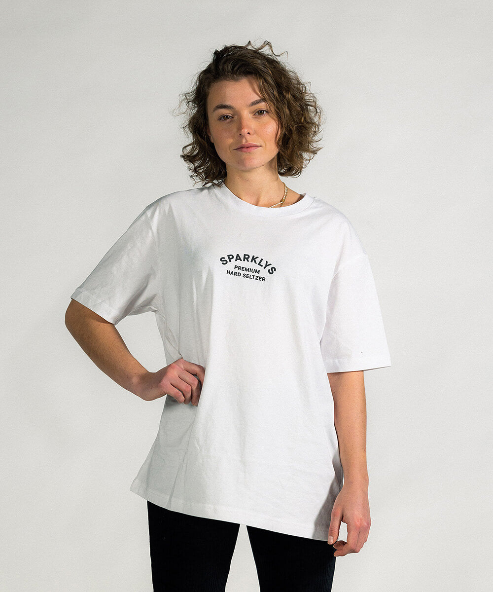 Weibliches Model präsentiert die Vorderseite des weissen Baumwoll-T-Shirts von Sparklys mit dem Vintage-Logo von Sparklys Premium Hard Seltzer auf der Brust.