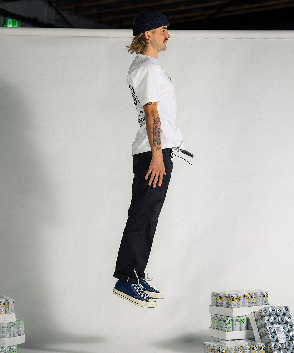 Dynamisches Foto eines männlichen Models, das in der Luft springt, während es das weisse Baumwoll-T-Shirt von Sparklys trägt, zeigt die Seitenansicht des T-Shirts und vermittelt einen energiegeladenen Eindruck.