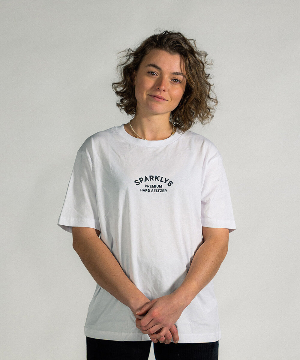 Weibliches Model präsentiert die Vorderseite des weissen Baumwoll-T-Shirts von Sparklys mit dem Vintage-Logo von Sparklys Premium Hard Seltzer auf der Brust
